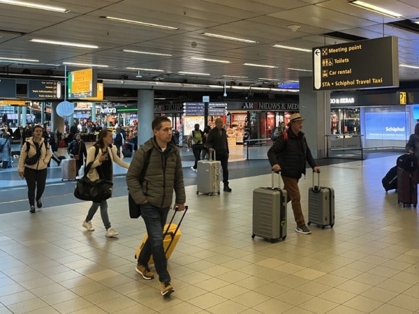 Travelers exiting Schiphol Airport baggage hall heading to their transfer to Amsterdam city center.