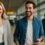 : Couple walking through Schiphol Airport arrivals hall towards their train transfer to Amsterdam city center