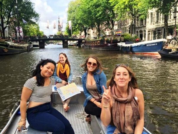 Young group of friends posing on an Amsterdam boat tour, with one holding a city map and an authentic canal in the background.
