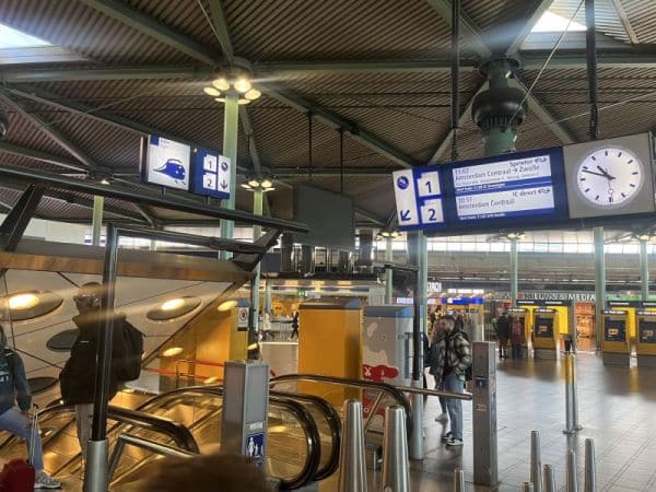 Signs inside Schiphol Airport showing directions to the train station for public transport to Amsterdam city center.